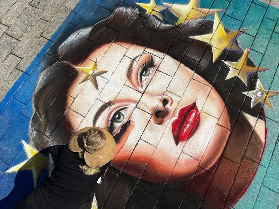 Chalk portrait of a woman with red lips and gold stars in her dark hair, Jessi drawing beside it