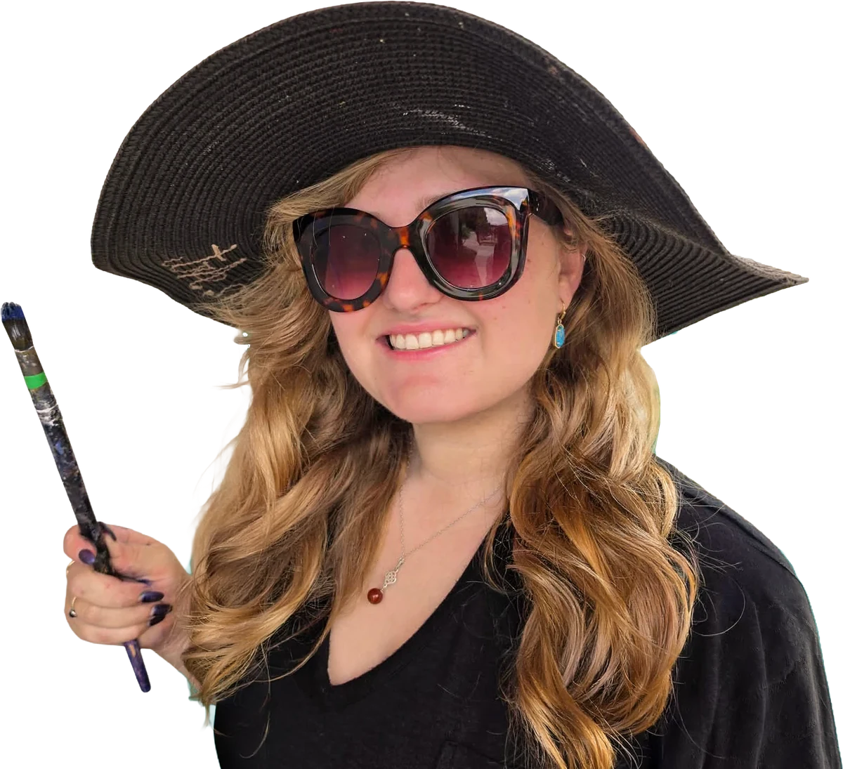Jessi Queen smiling in a wide-brimmed black hat and tortoiseshell sunglasses, holding a paintbrush