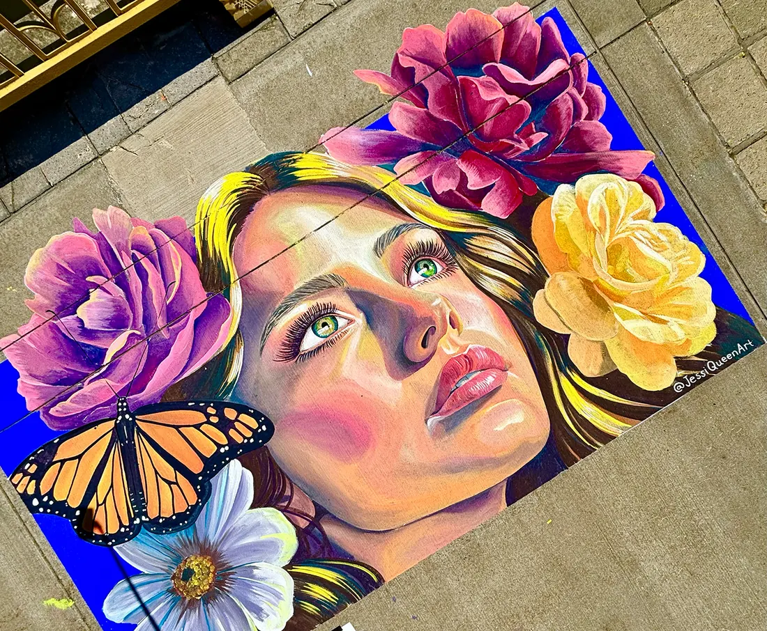 Street chalk portrait of a woman gazing upward, framed by pink and yellow roses and a monarch butterfly
