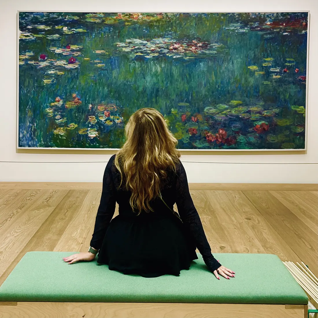 Jessi seated on a museum bench in front of a large water lily painting