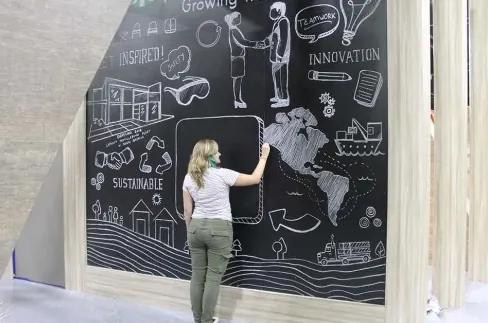Jessi drawing a sustainability-themed chalk mural with a world map on a large blackboard wall
