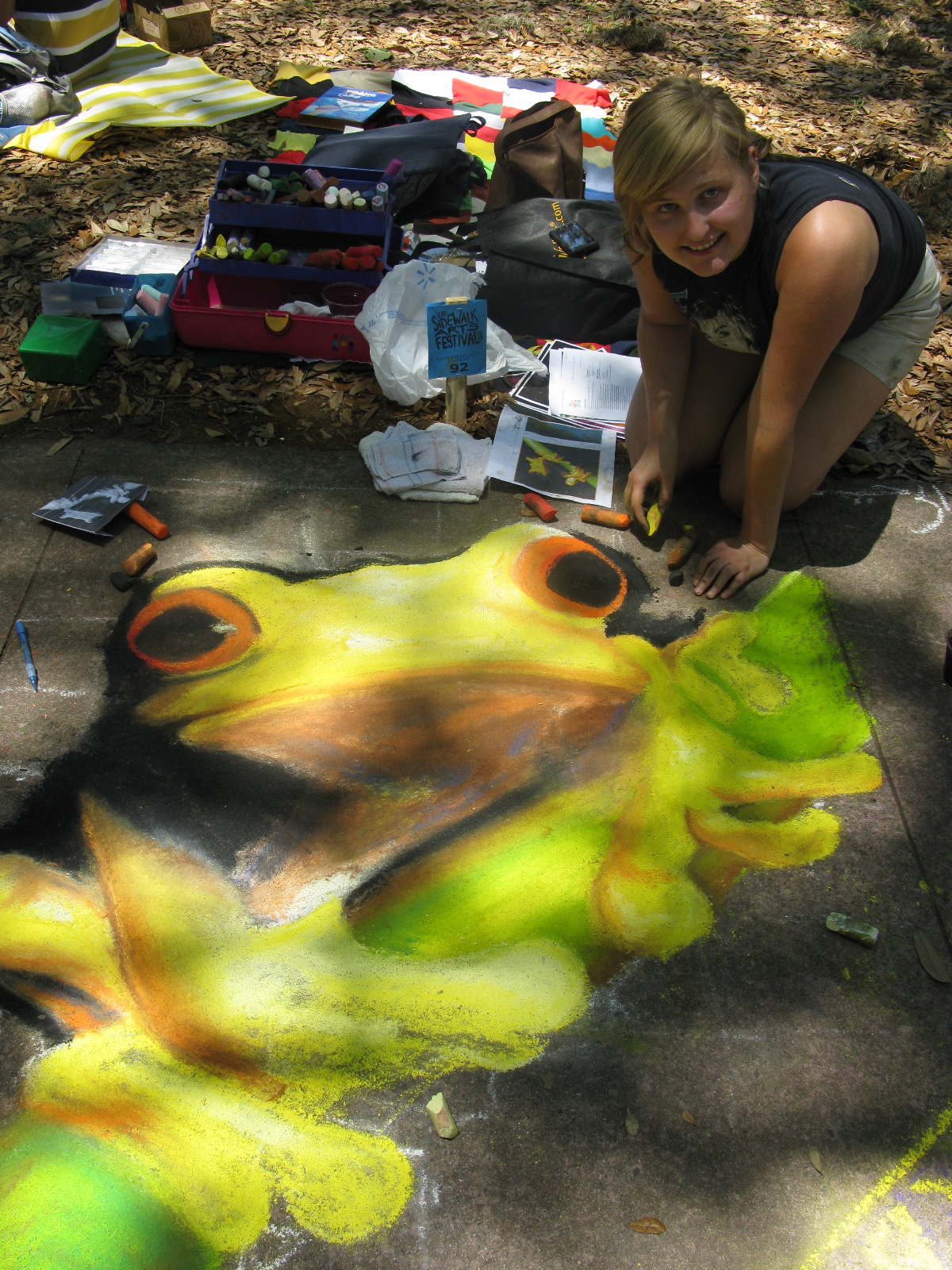 Jessi kneeling beside her chalk drawing of a bright green tree frog