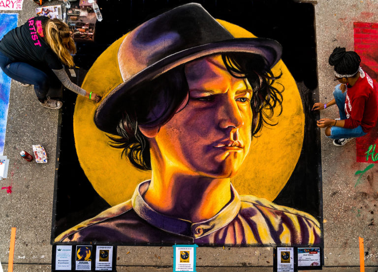 The finished chalk portrait of a young man in a black hat against a golden sun, from above