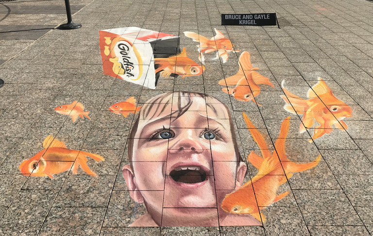 Finished 3D chalk mural of a laughing child as goldfish crackers pour from a Goldfish box