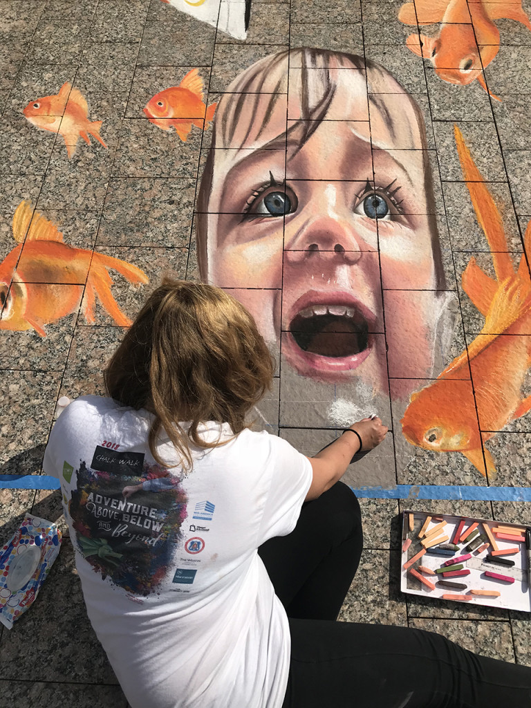 Jessi drawing a 3D chalk mural of a laughing child surrounded by goldfish crackers