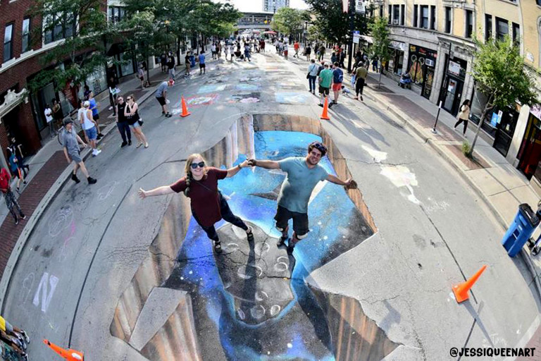 Two people appearing to leap over a 3D chalk crevasse opening into outer space on a city street
