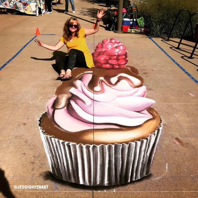 Woman waving while seated behind a giant 3D chalk cupcake topped with a raspberry