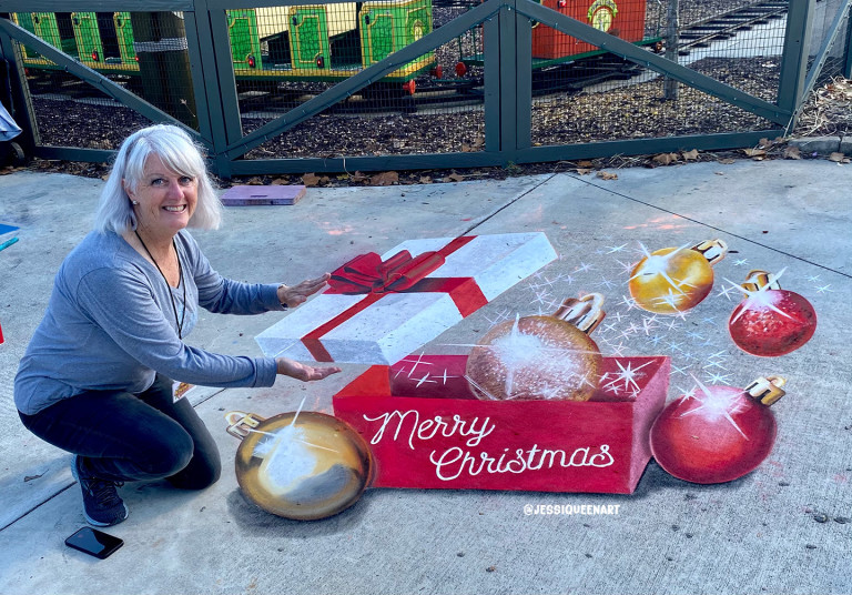 Woman reaching for a 3D chalk Christmas gift box surrounded by ornaments reading Merry Christmas