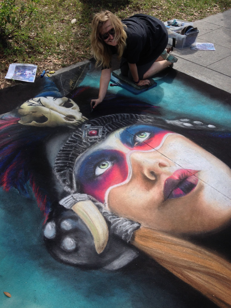 Jessi kneeling at the edge of her chalk portrait, blending the teal background