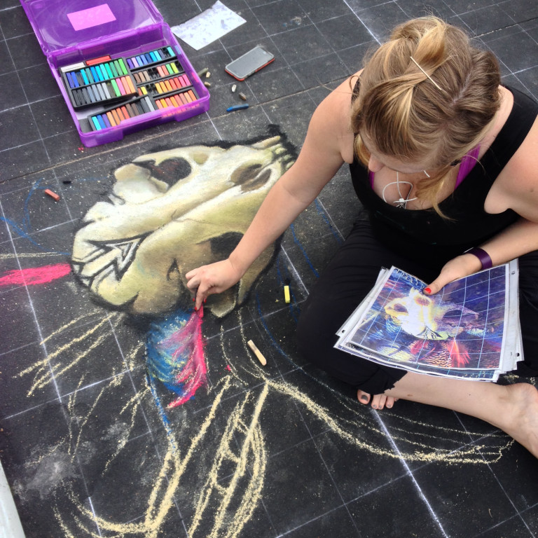 Jessi early in the drawing, sketching the skull and headdress over a chalk grid, with her reference print beside her