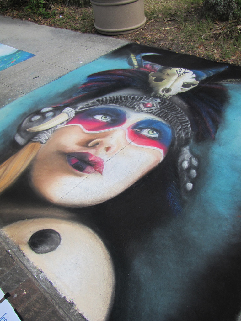 The finished chalk portrait of a woman in a feathered headdress with a skull ornament and red and blue face paint