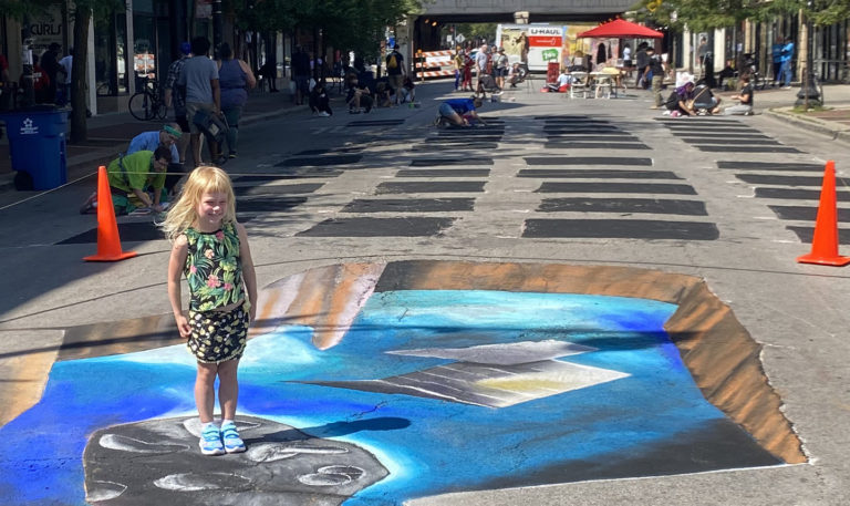 Young girl standing at the edge of a 3D chalk hole that opens into outer space on a festival street
