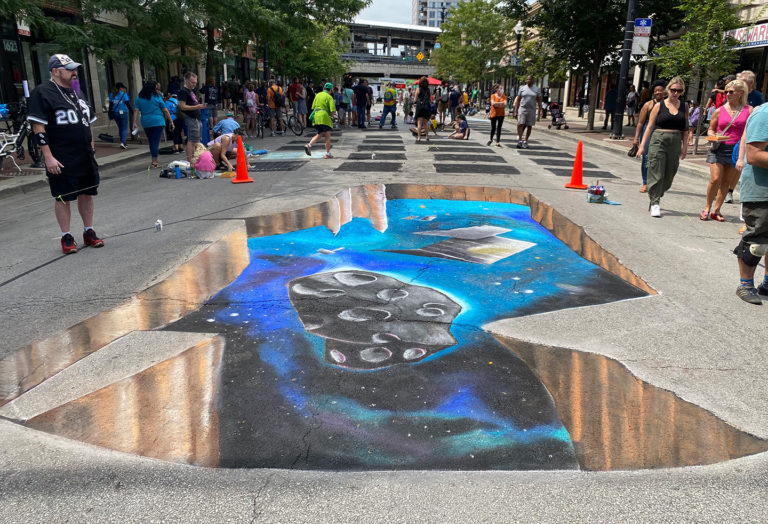 3D chalk illusion of a hole in the street revealing a galaxy and a floating asteroid