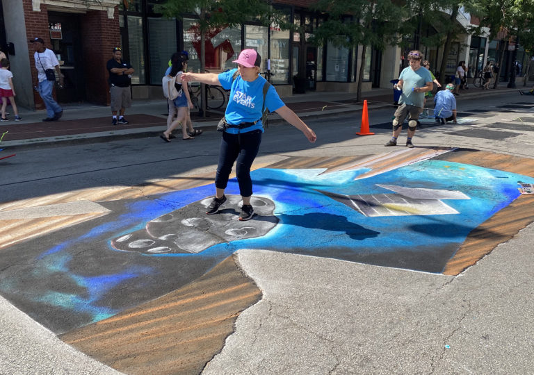 Visitor balancing on the asteroid in the 3D galaxy-in-a-hole chalk mural