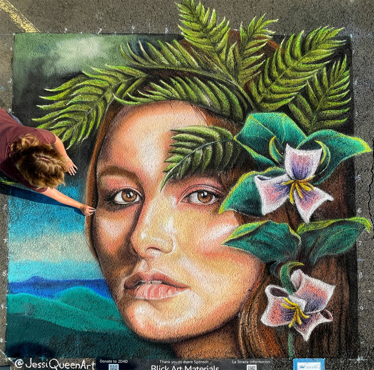 Jessi drawing a chalk portrait of a woman crowned with ferns and white trillium flowers