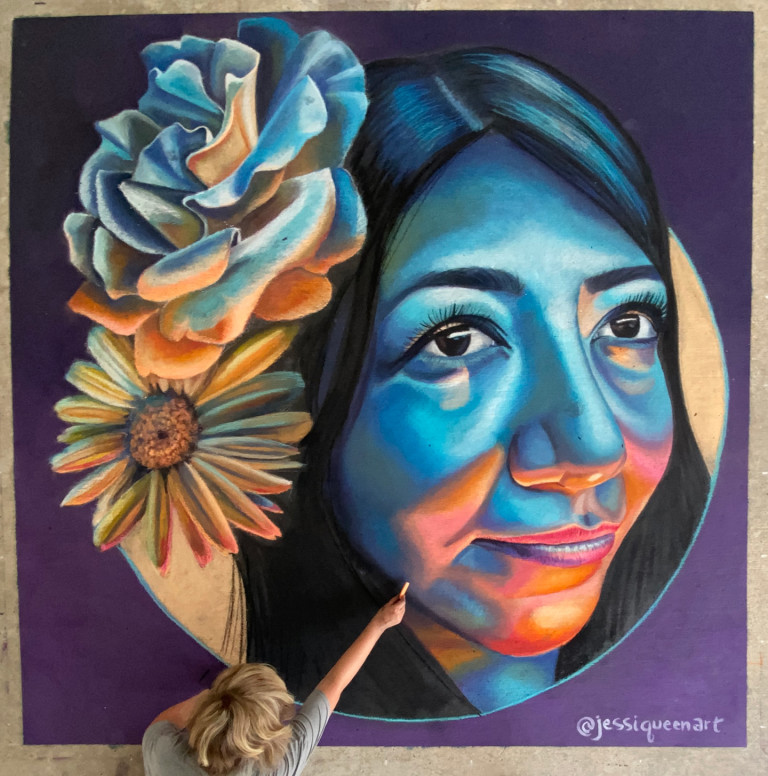 Jessi drawing a chalk portrait of a woman in vivid blues and oranges with a large rose and sunflower