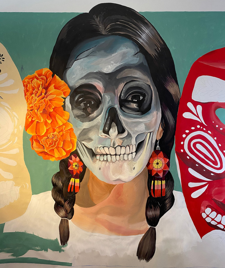 Dia de los Muertos mural of a woman with a skull face, braids, and orange marigolds