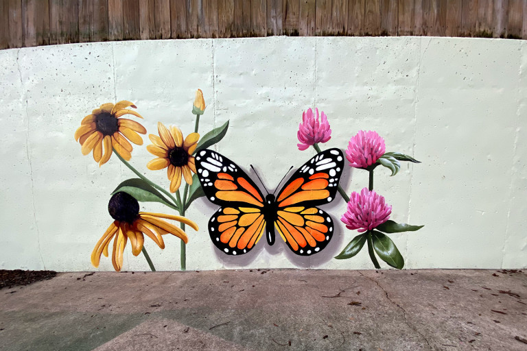 Painted wall mural of a monarch butterfly among black-eyed Susans and pink clover