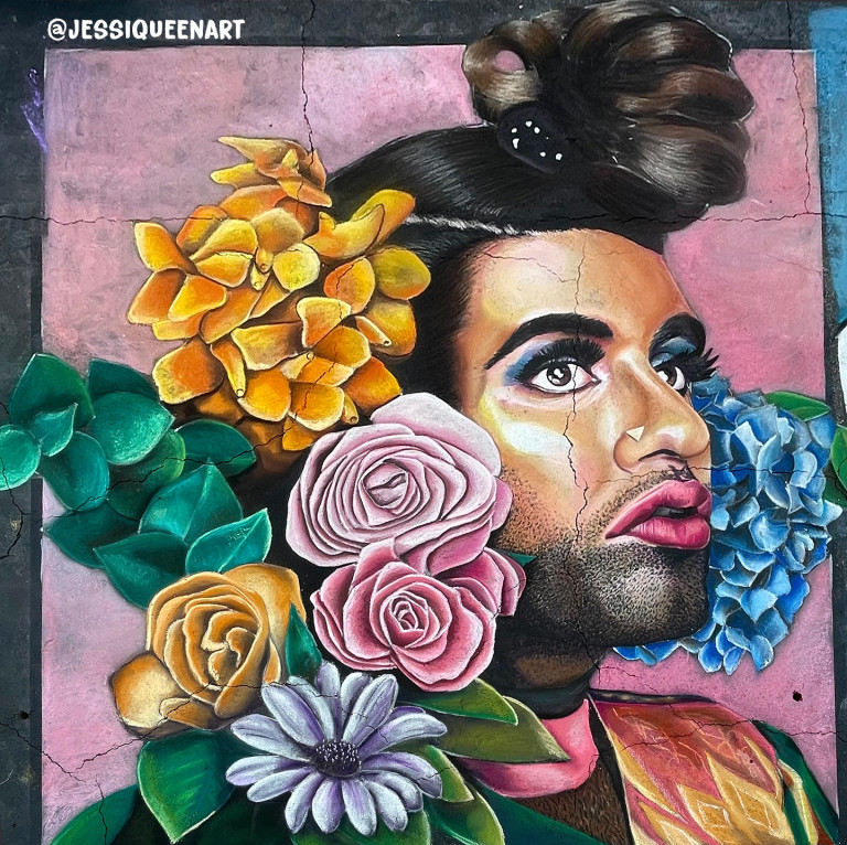 Chalk portrait of a man in dramatic makeup surrounded by roses, daisies and blue hydrangeas on pink