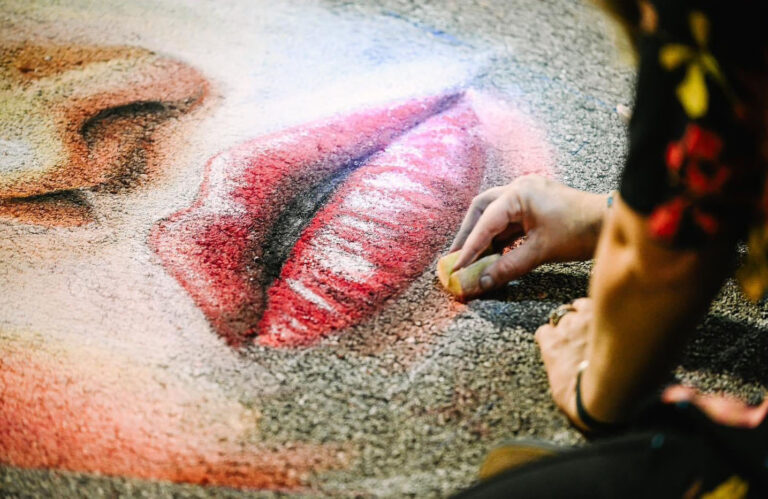 Close-up of a hand blending red chalk on the lips of a large street portrait