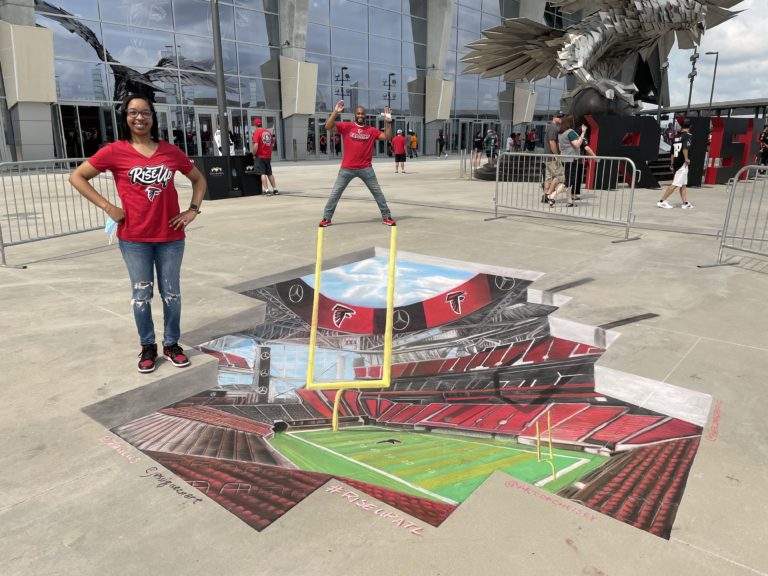 Two Falcons fans posing on a 3D chalk mural of the stadium field and goalposts