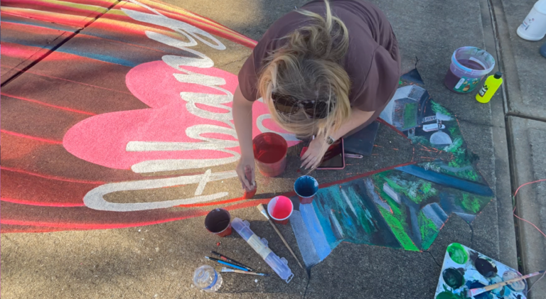 Jessi chalking the Albany lettering on a pink heart for a 3D mural