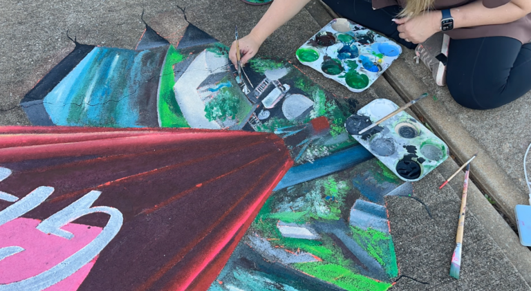 Chalk palettes and brushes beside a river landscape being drawn at the base of the Albany heart