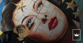 Jessi Queen creating a large-scale chalk portrait mural on a brick surface.