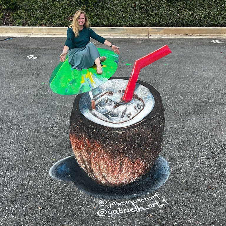 Jessi seated on the umbrella of a giant 3D chalk coconut drink with a red straw