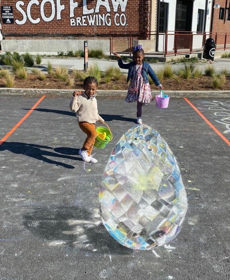 Two children with Easter baskets hopping toward a giant 3D chalk crystal egg outside Scofflaw Brewing