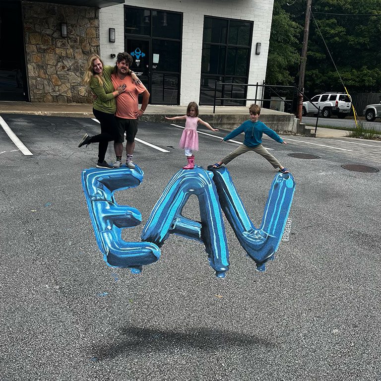 Jessi and family posing on giant 3D chalk blue balloon letters spelling EAV