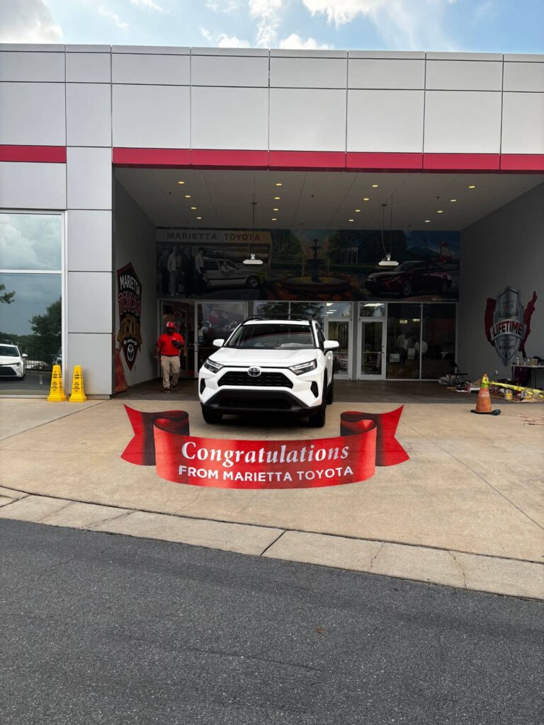 3D chalk red ribbon reading Congratulations from Marietta Toyota in front of a new SUV
