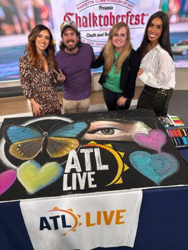 Jessi and a fellow chalk artist with ATL Live hosts Ava and Savannah behind a chalk drawing of a butterfly, an eye, hearts and the ATL Live logo, in front of a Chalktoberfest 2026 backdrop