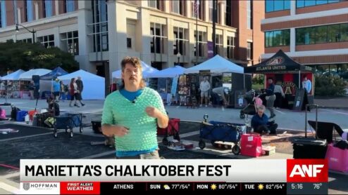 Still from the Atlanta News First segment: Zach Herndon being interviewed on the Marietta Square during Chalktoberfest 2025, with artists chalking behind him