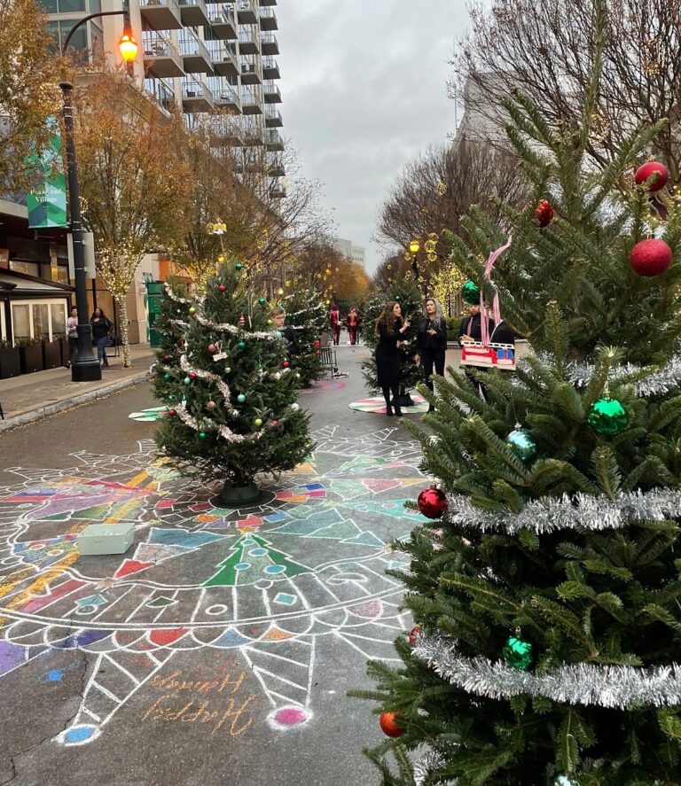 Street lined with decorated Christmas trees above a colorful chalk mandala reading Happy Holidays at Buckhead Village