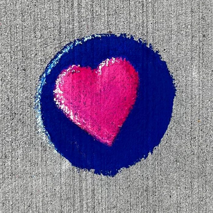 Small chalk drawing of a pink heart inside a deep blue circle on a sidewalk