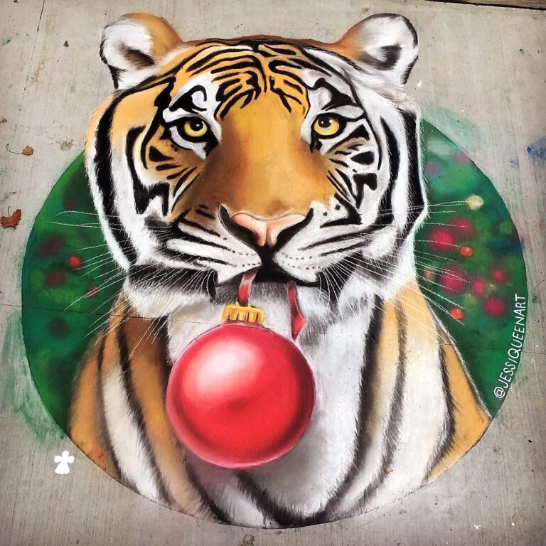 Chalk tiger holding a red Christmas ornament in its mouth by a ribbon, framed by a green circle of festive lights