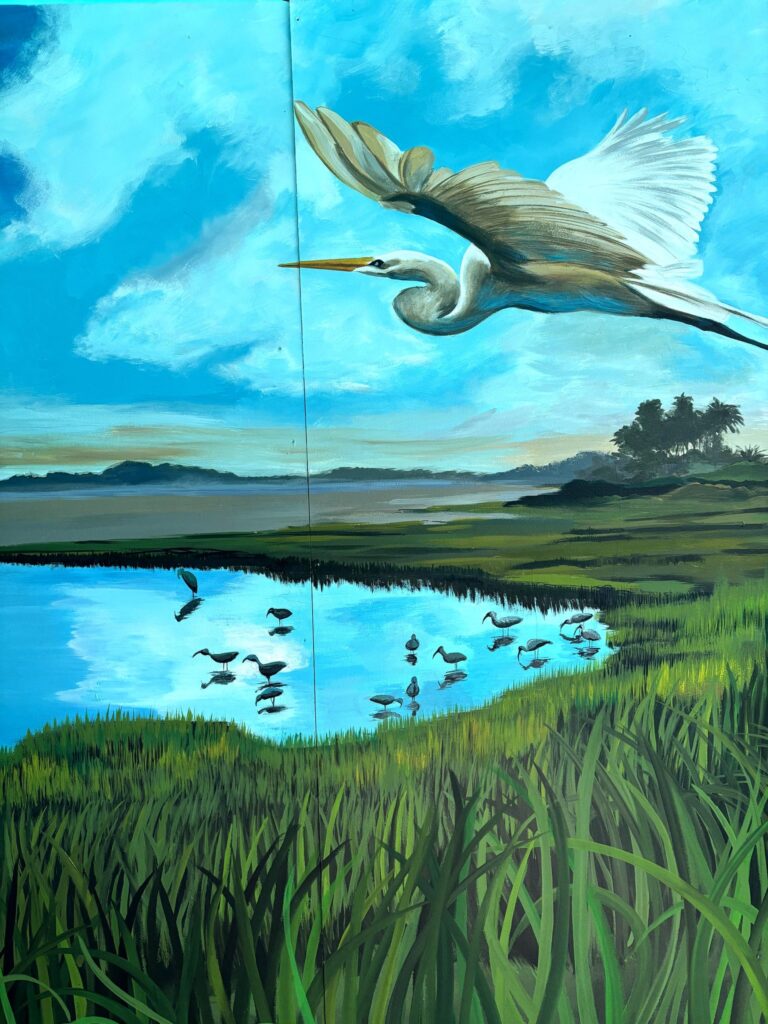 Painted mural of a great egret flying over a coastal marsh, with wading ibises reflected in blue water and tall grasses in front