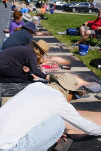 A row of artists kneeling along the memorial walkway, each chalking a portrait beside the grass