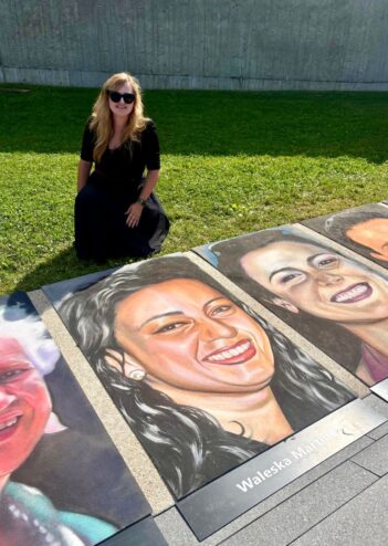 Jessi kneeling on the grass beside her chalk portrait of Waleska Martinez on the memorial walkway