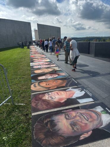 Visitors walking along the line of chalk portraits between the tall concrete walls of the Flight 93 National Memorial