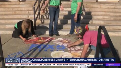 Still from the FOX 5 Good Day Atlanta segment: Jessi and Zach Herndon chalking the poppy and daisies around the FOX 5 logo on the Marietta sidewalk, under the headline Annual Chalktoberfest draws international artists to Marietta