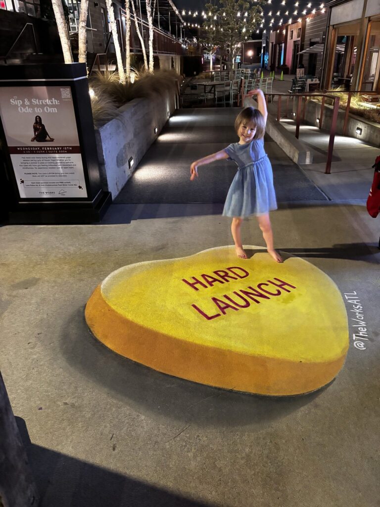 Young girl dancing on a 3D chalk yellow candy heart reading Hard Launch at night