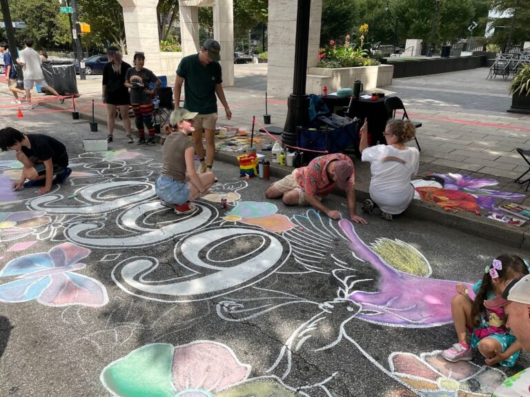 Volunteers coloring a large community chalk mural of flowers and birds on a closed Midtown street