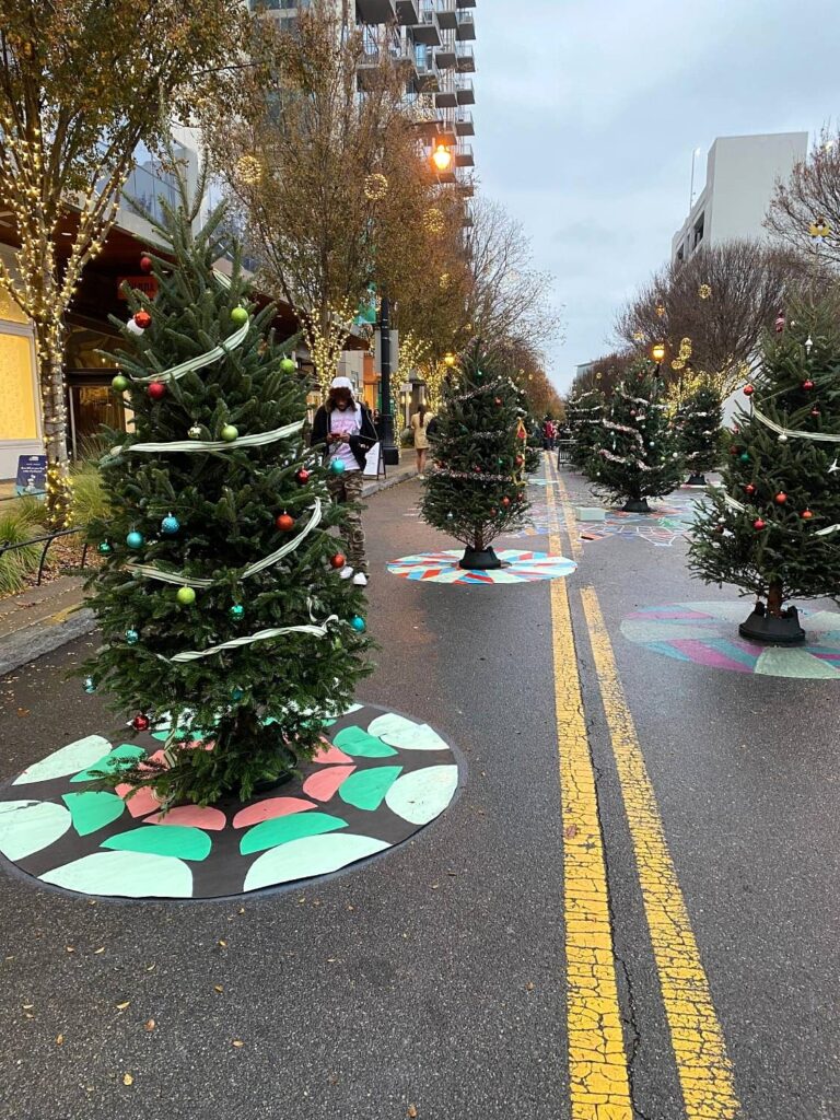 Christmas tree with a mint, coral and black painted tree skirt, with more patterned skirts down the street
