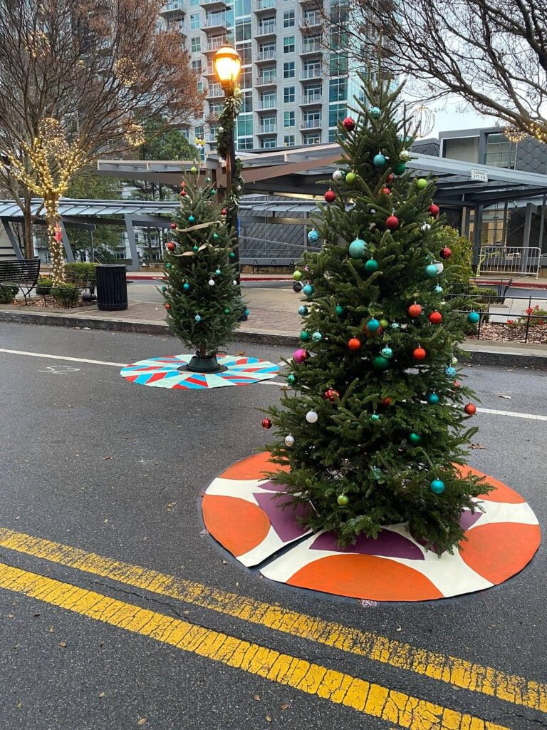 Decorated Christmas trees standing on painted tree skirts in orange, cream and plum and in red and blue stripes