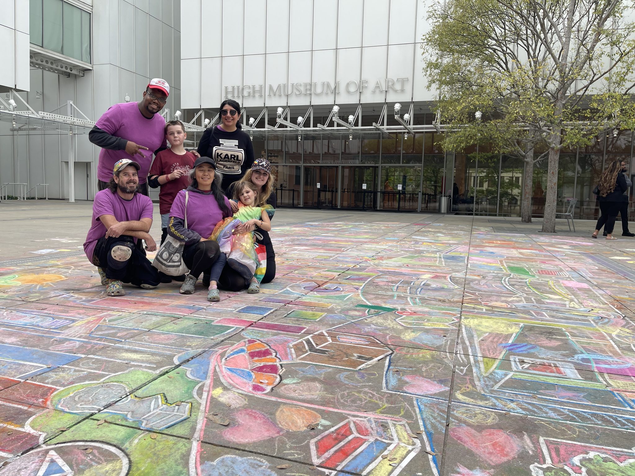 Jessi, Zach and friends in purple Artist shirts posing on the finished chalk drawing in front of the High Museum of Art